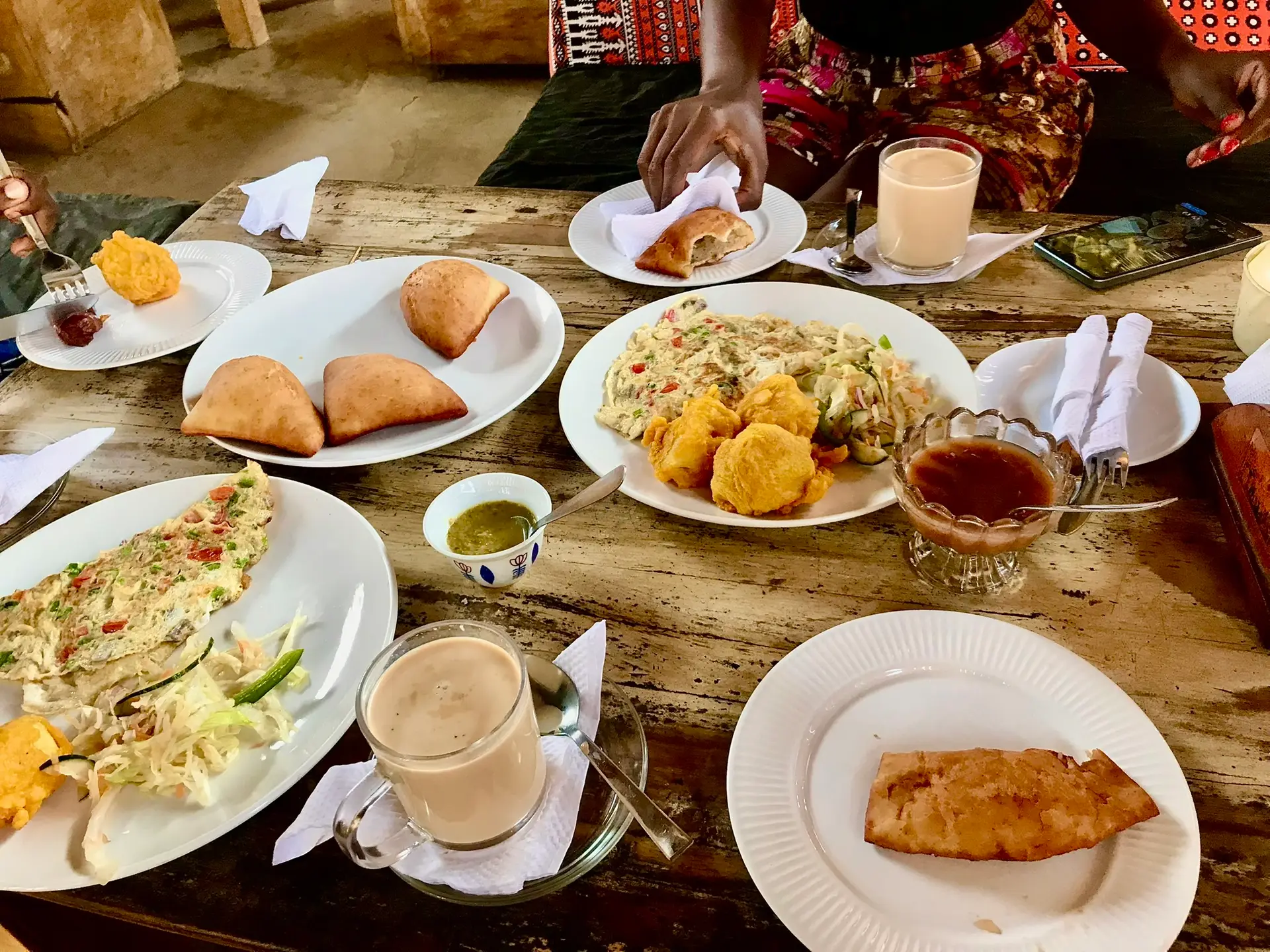 Breakfast food on a table including omelette, Mahamri and milk tea. 